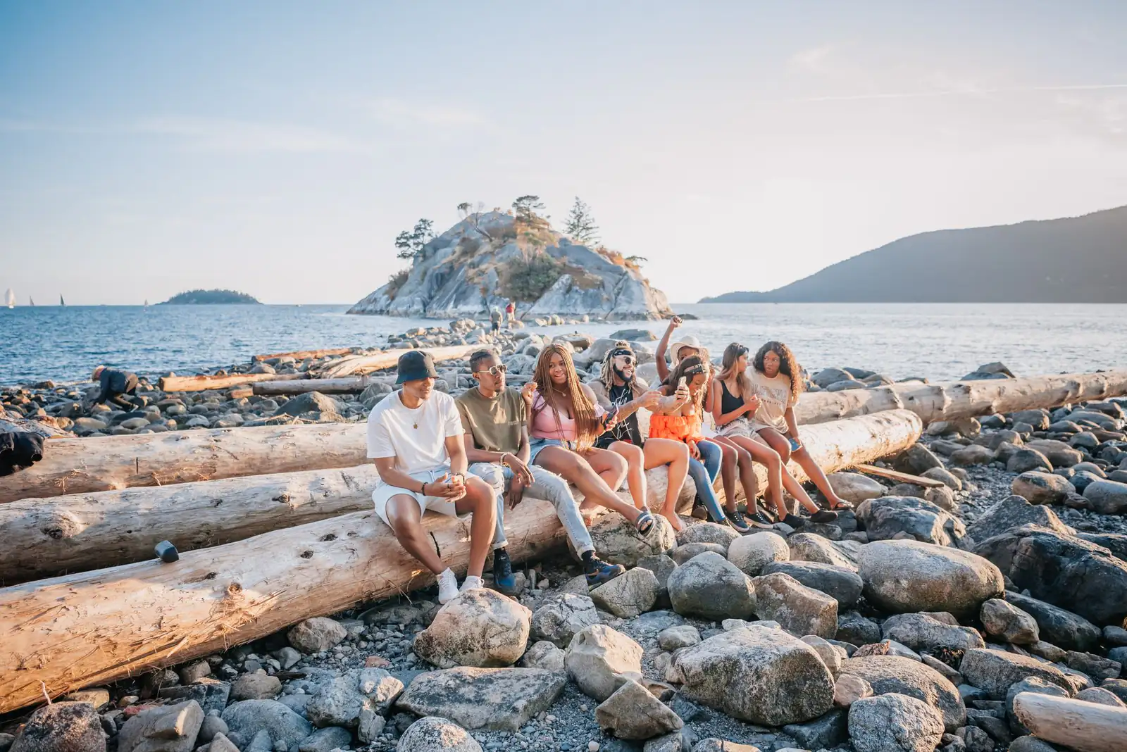 Friends sitting together on driftwood logs on a rocky beach near Vancouver