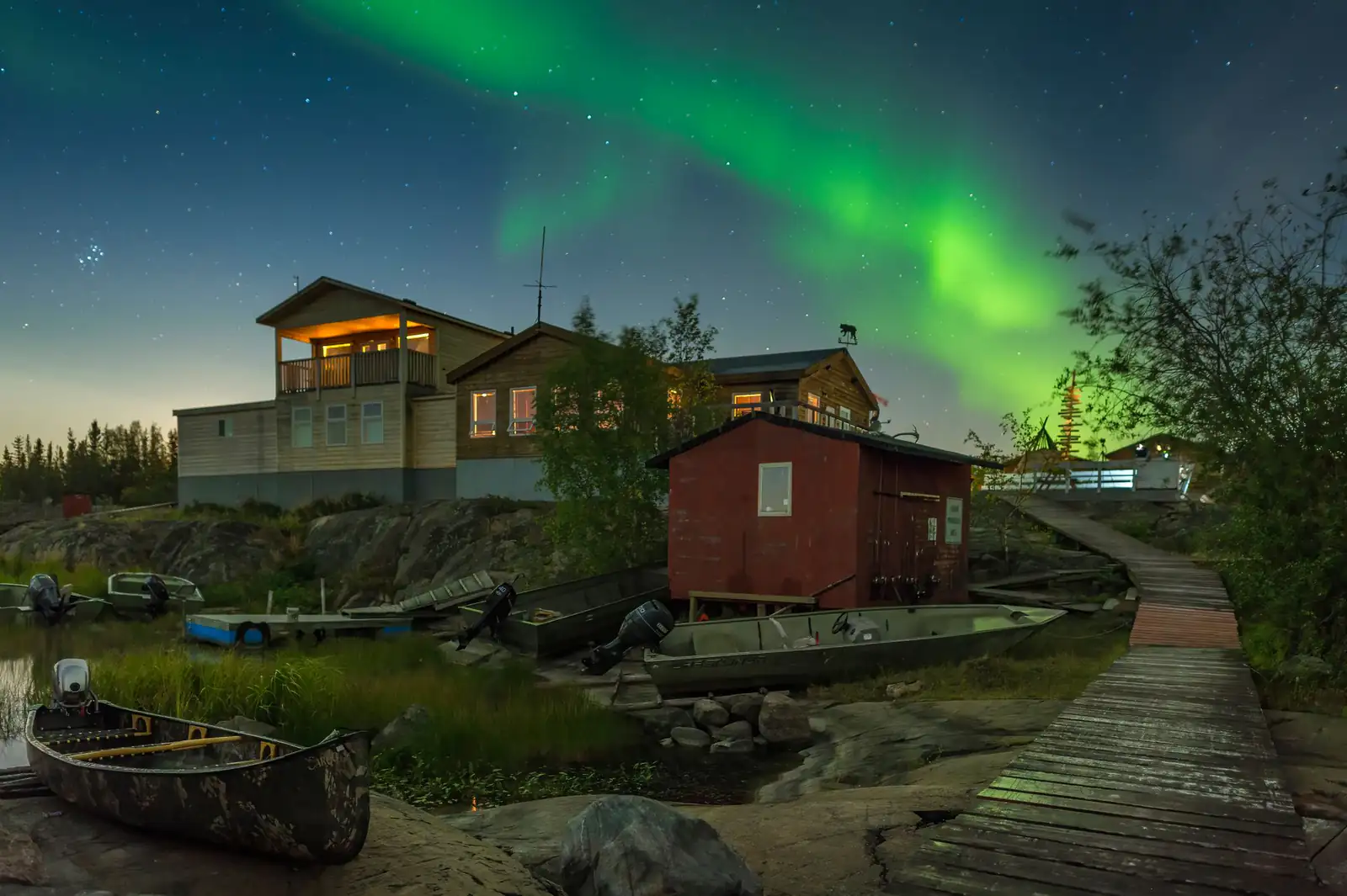 Green northern lights above houses on the rocky shore in Yellowknife